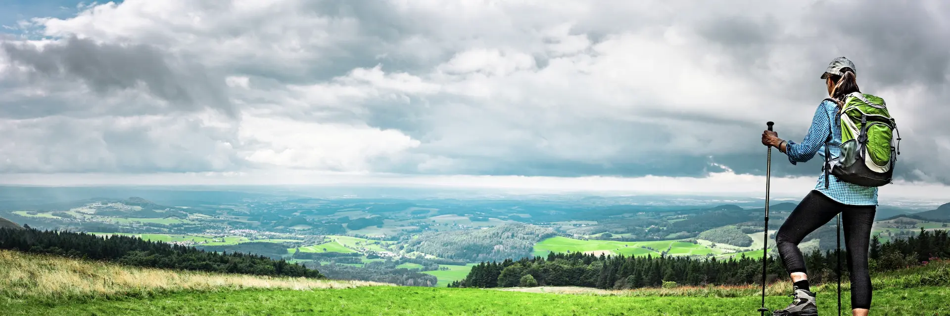 Wanderin mit Rucksack und Trekkingstöcken auf einer Anhöhe mit weitem Blick über die Landschaft der Rhön