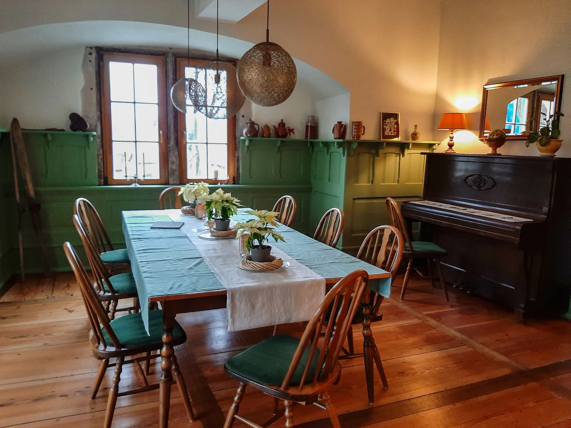 Gemütlicher Bereich der Bibliothek im Schloß Roßdorf mit großem Holztisch, Stühlen, historischem Klavier und warmem Licht