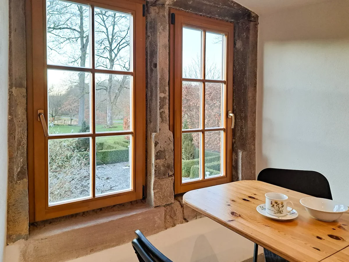 Essplatz der Ferienwohnung von Roßdorf im Schloß Roßdorf mit Holztisch, Fenstern und Blick ins Grüne