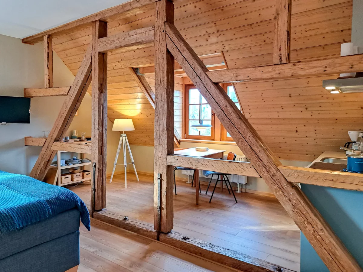 Wohnbereich der Ferienwohnung von Eschwege im Schloß Roßdorf mit sichtbaren Holzbalken, Sitzbereich, Esstisch und Küchenzeile