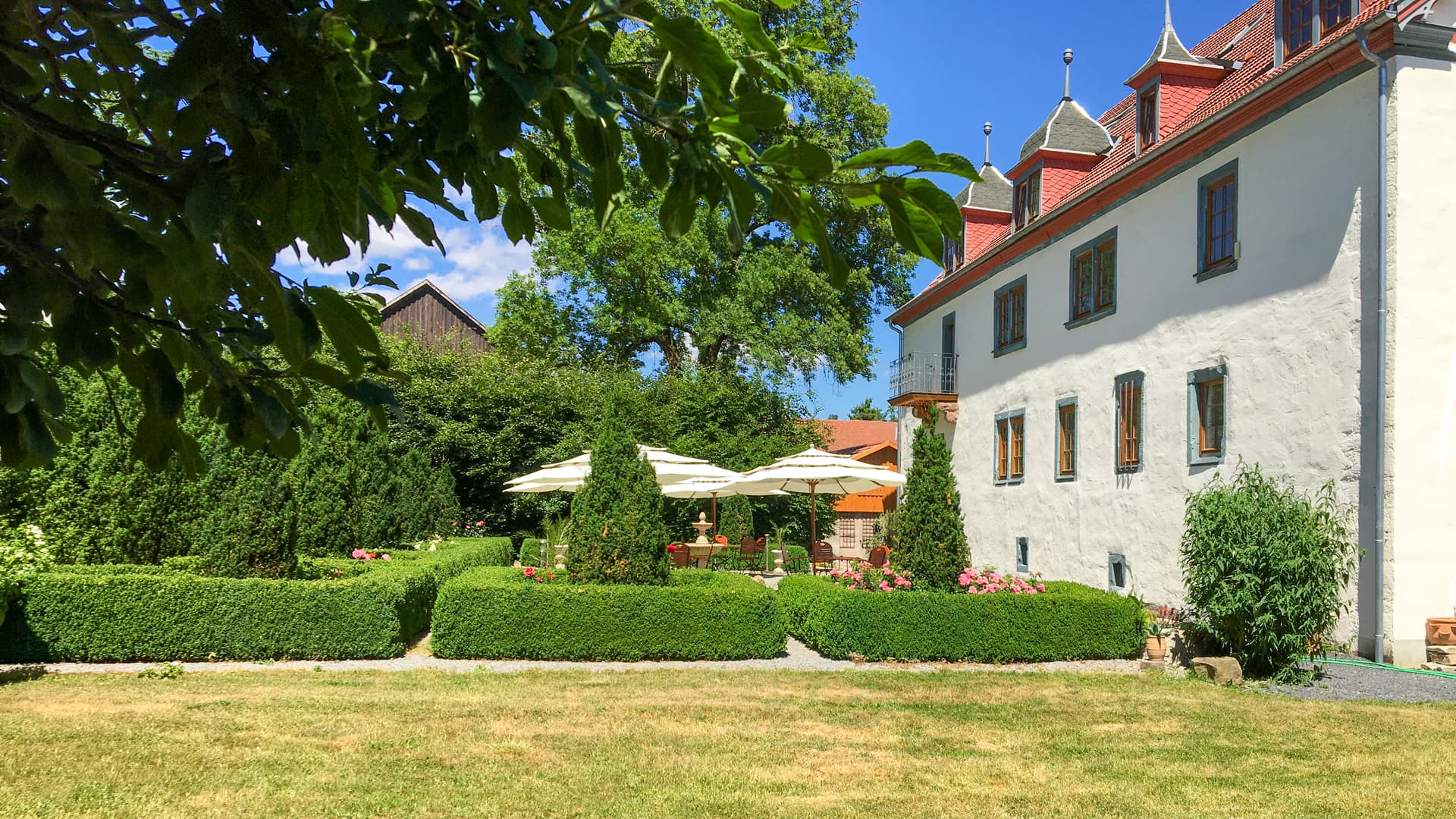 Außenansicht von Schloß Roßdorf mit gepflegter Gartenterrasse, Sonnenschirmen und ruhiger Gartenanlage